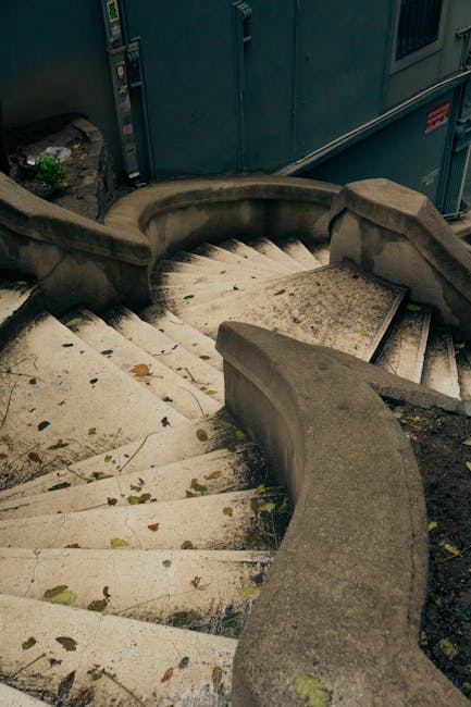 Image of a narrow industrial staircase with yellow and black striped safety markings on each step, leading up to a higher level within a building structure. The staircase has metal railings painted yellow, positioned on both sides, and features a sign on the steps that reads 'PLEASE KEEP LEFT'. The surrounding environment includes metal beams and industrial equipment, with lighting casting shadows on the steps. This setting emphasizes the importance of maintaining cleanliness and safety in challenging access areas, reflecting the expertise of Harrow Carpet Cleaners in thorough surface cleaning and sanitation for commercial or residential spaces, especially in hard-to-reach locations such as narrow stairs in flats or industrial buildings.